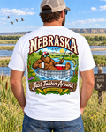Nebraska Bigfoot shirt with Sasquatch floating in a livestock tank on a river with fishing gear, prairie scenery, corn, and Cornhusker State artwork.
