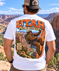 Utah Bigfoot Take the Scenic Route shirt featuring Sasquatch rappelling through a colorful red rock canyon landscape.